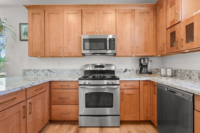 kitchen with stainless steel appliances, light wood-style flooring, and light stone countertops