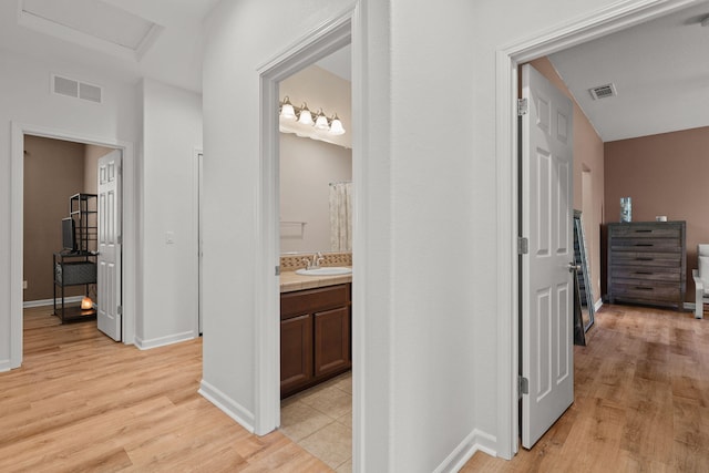 hallway featuring light wood-style floors, visible vents, baseboards, and a sink