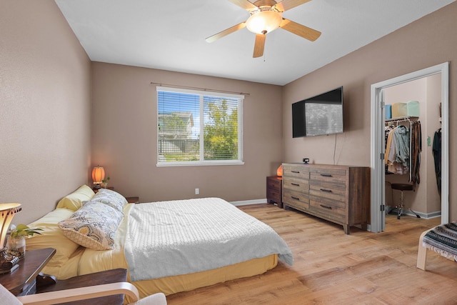 bedroom featuring a closet, light wood-style flooring, baseboards, ceiling fan, and a walk in closet