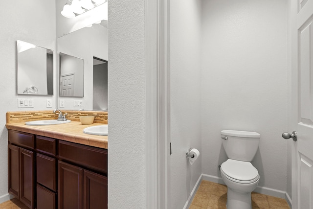 bathroom featuring double vanity, toilet, a sink, baseboards, and tile patterned flooring