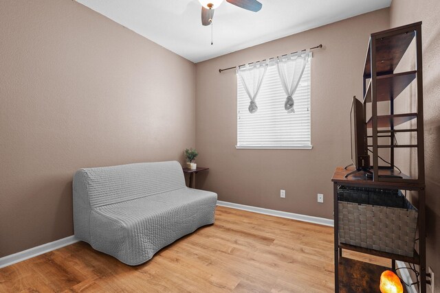 living area with baseboards, a ceiling fan, and wood finished floors