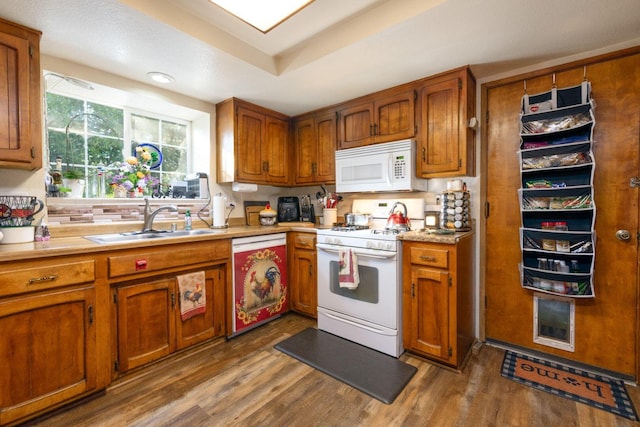 kitchen featuring white appliances, brown cabinets, a sink, and wood finished floors