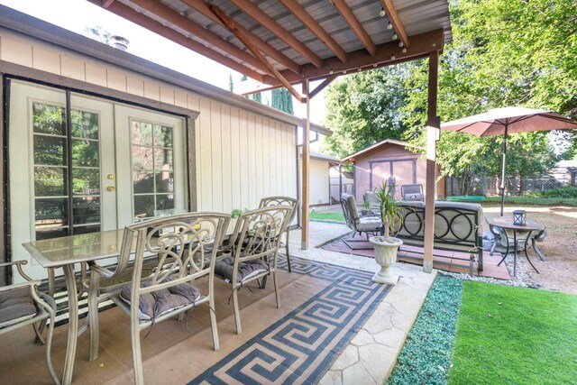 view of patio with fence, outdoor dining space, a shed, french doors, and an outdoor structure