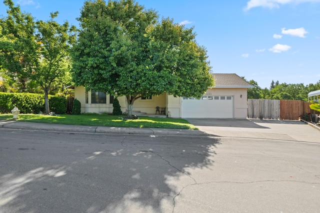 view of property hidden behind natural elements featuring a garage, a front lawn, fence, stucco siding, and concrete driveway