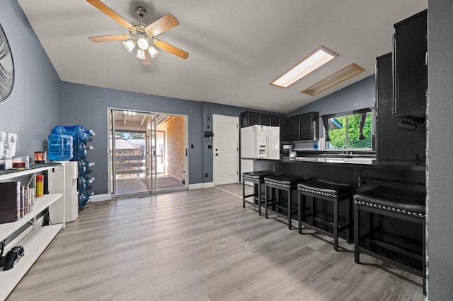 kitchen featuring white fridge with ice dispenser, light wood finished floors, lofted ceiling, dark cabinetry, and a breakfast bar