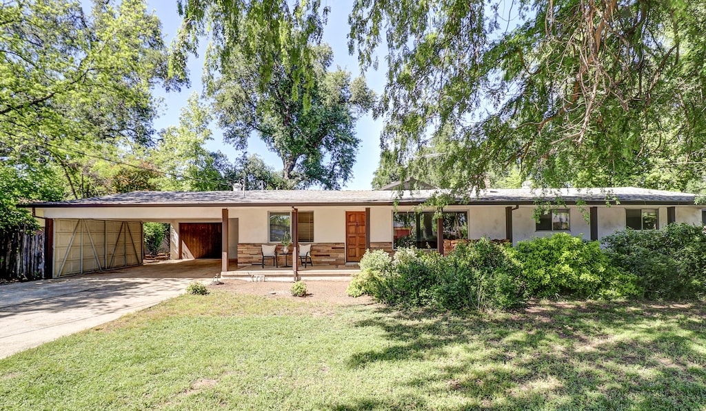 ranch-style home with a front lawn, stucco siding, an attached carport, a porch, and driveway