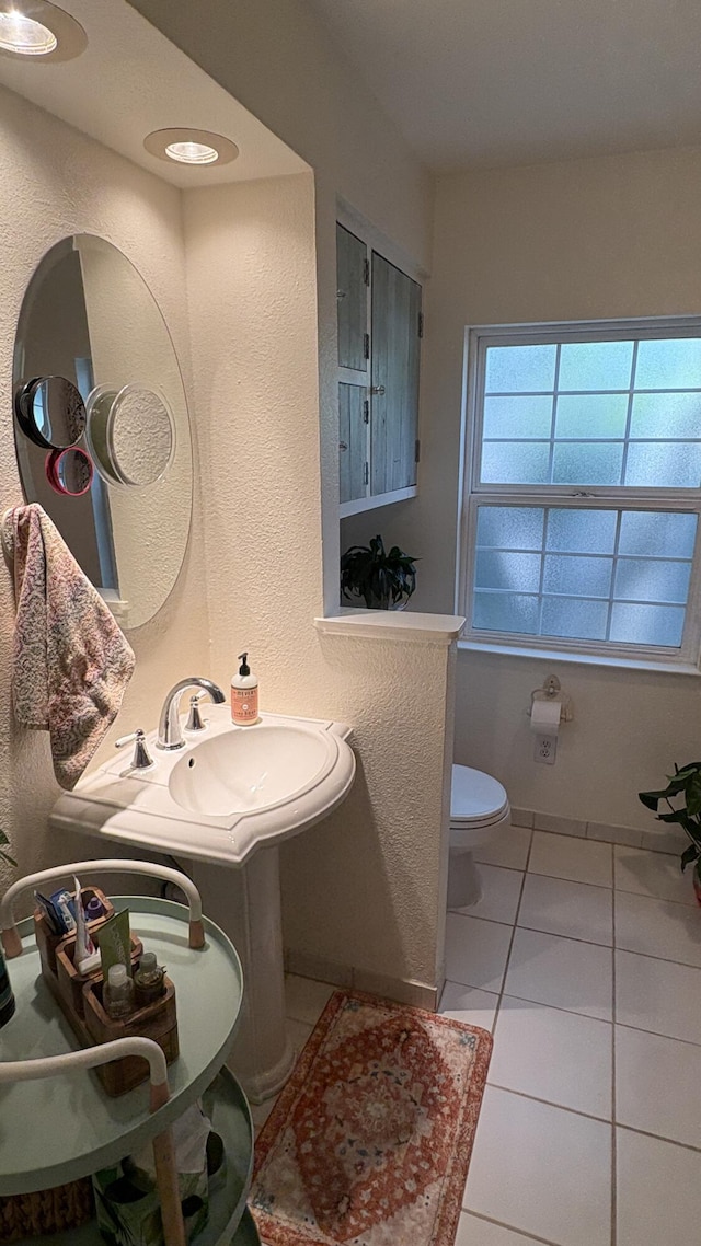half bath featuring toilet, a textured wall, a sink, and tile patterned flooring