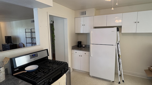 kitchen featuring stainless steel range with gas stovetop, freestanding refrigerator, white cabinetry, and visible vents