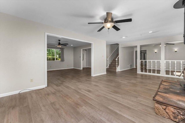unfurnished living room featuring wood finished floors, a ceiling fan, visible vents, baseboards, and stairs