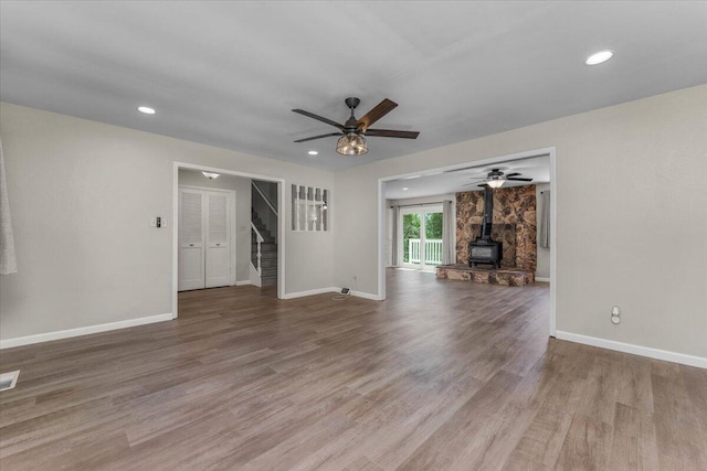 unfurnished living room featuring wood finished floors, a ceiling fan, stairway, baseboards, and a wood stove