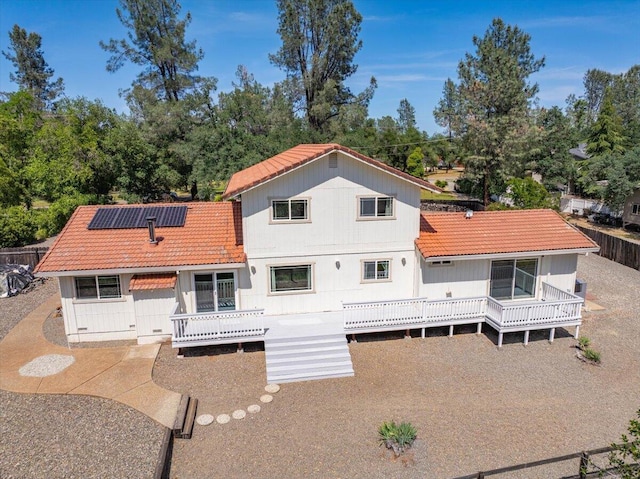 rear view of house with a deck, a tiled roof, solar panels, and fence
