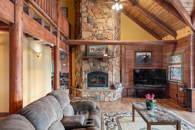 living area with a stone fireplace, ceiling fan, wood ceiling, wood finished floors, and beamed ceiling