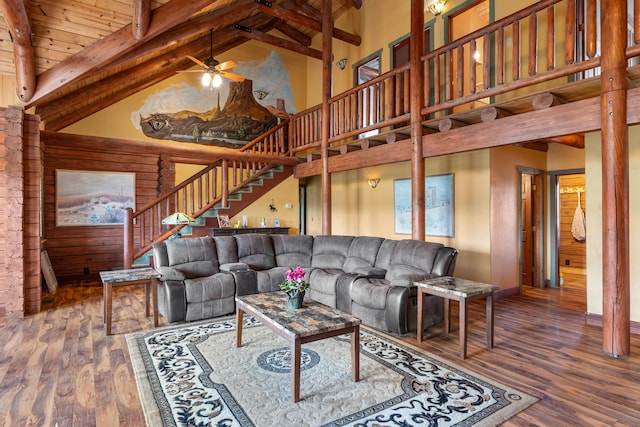 living area featuring beam ceiling, high vaulted ceiling, wood finished floors, and stairs