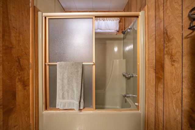 bathroom with wooden walls and combined bath / shower with glass door