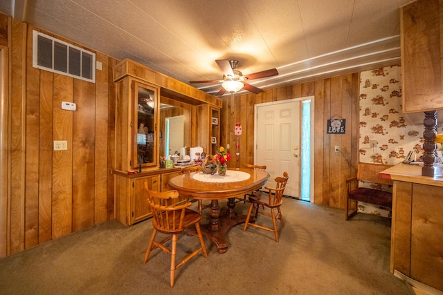 dining room with a ceiling fan, wood walls, visible vents, and carpet floors