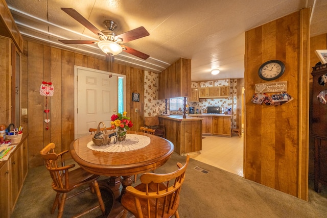 dining room featuring visible vents, wood walls, ceiling fan, and light carpet