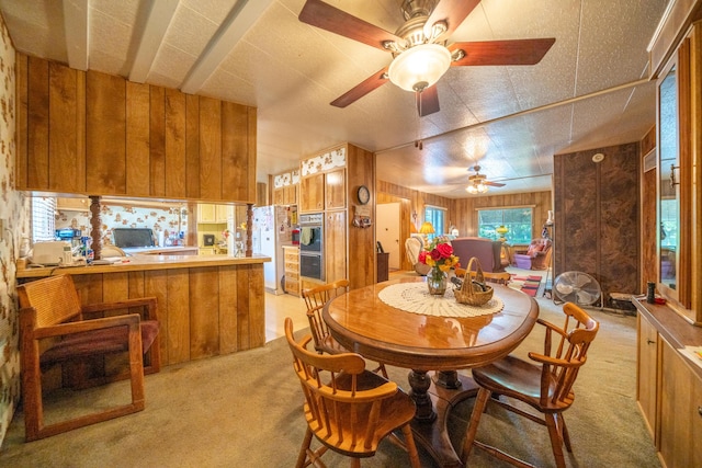 dining area with a ceiling fan, wooden walls, and light colored carpet