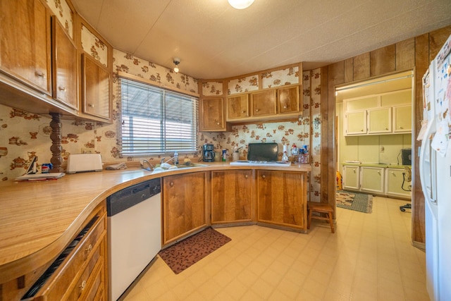 kitchen featuring brown cabinets, light countertops, white dishwasher, and wallpapered walls