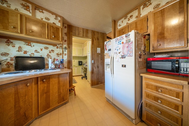 kitchen featuring white fridge with ice dispenser, brown cabinets, black microwave, and light floors