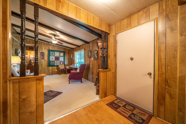 entrance foyer with wooden walls, lofted ceiling with beams, a ceiling fan, and wood finished floors