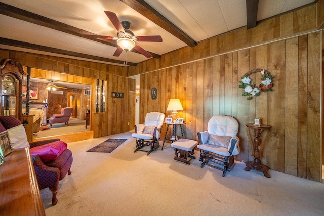 sitting room featuring beamed ceiling, wood walls, ceiling fan, and carpet