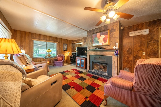 carpeted living area featuring a large fireplace, wood walls, and a ceiling fan