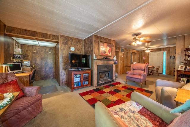 carpeted living area featuring wood walls, ceiling fan, a fireplace with raised hearth, and visible vents