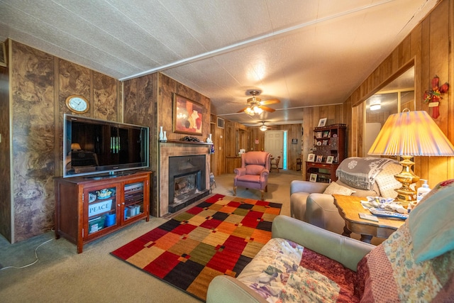 living room with wooden walls, a fireplace, ceiling fan, and carpet floors