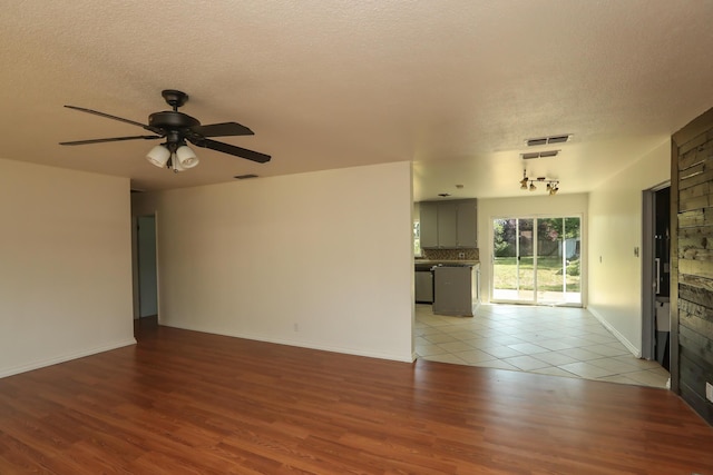 unfurnished living room featuring visible vents, a ceiling fan, a textured ceiling, and light wood-style flooring