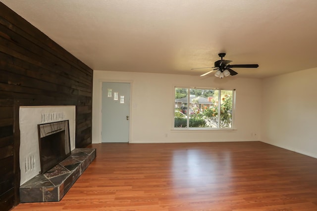 unfurnished living room with a tiled fireplace, baseboards, ceiling fan, and wood finished floors