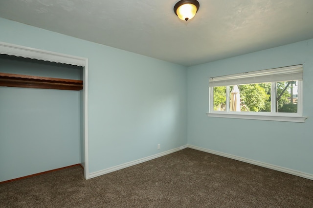 unfurnished bedroom featuring baseboards, a closet, and dark carpet