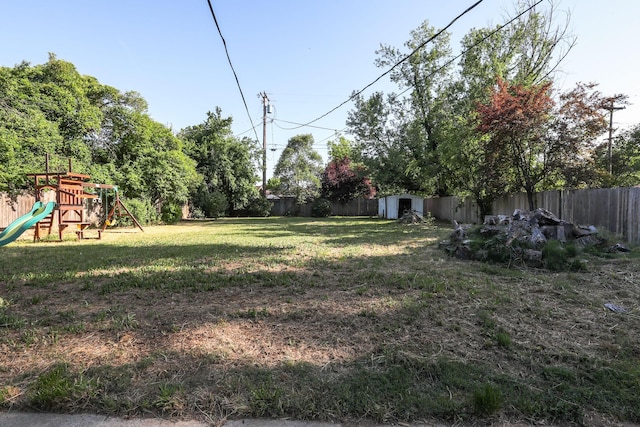 view of yard featuring an outdoor structure, a fenced backyard, a playground, and a storage shed