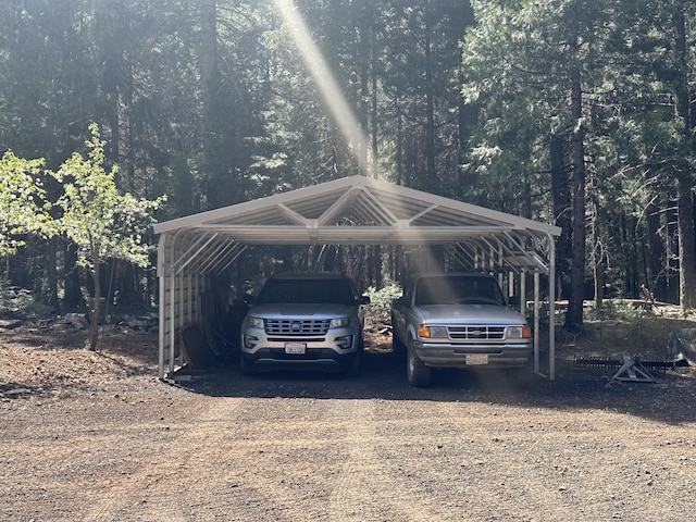view of parking / parking lot with a detached carport, driveway, and a forest view