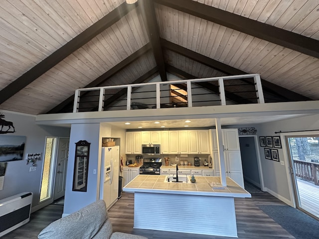 kitchen featuring baseboards, high vaulted ceiling, tile countertops, a sink, and appliances with stainless steel finishes