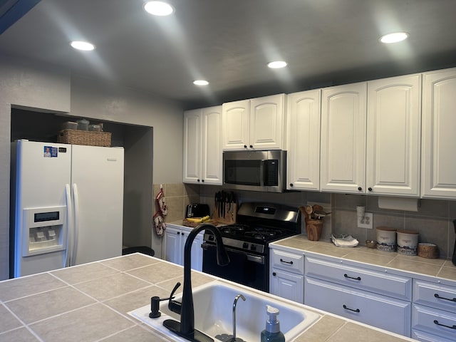 kitchen featuring appliances with stainless steel finishes, a sink, tile counters, white cabinetry, and backsplash