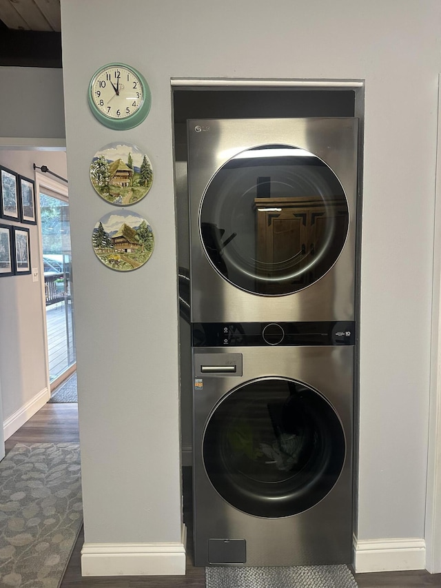 laundry area with baseboards, stacked washer and dryer, laundry area, and wood finished floors
