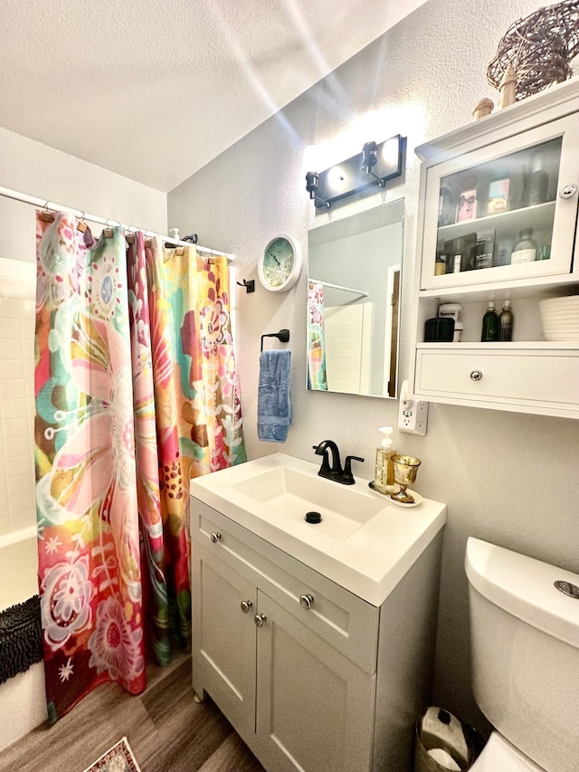 bathroom with a textured wall, vanity, toilet, a textured ceiling, and wood finished floors