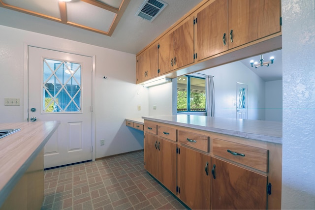 kitchen with brown cabinets, an inviting chandelier, light countertops, brick patterned floor, and visible vents