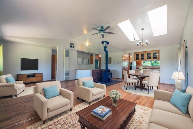 living room featuring a wood stove, ceiling fan with notable chandelier, wood finished floors, visible vents, and lofted ceiling with skylight