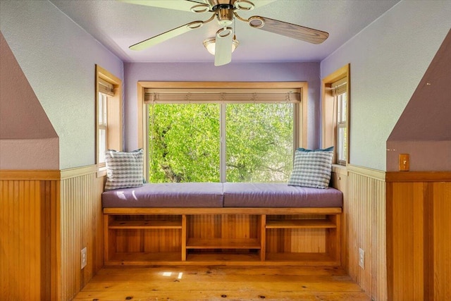 sitting room with a textured wall, a ceiling fan, wainscoting, and hardwood / wood-style flooring