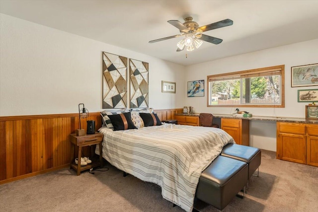 bedroom with light carpet, wooden walls, ceiling fan, and a wainscoted wall