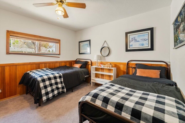 bedroom featuring light colored carpet, wooden walls, a wainscoted wall, and a ceiling fan