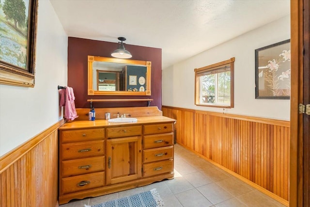 bathroom with a wainscoted wall, wood walls, tile patterned flooring, and vanity