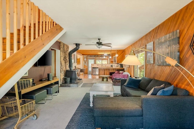 carpeted living area with wooden walls, a healthy amount of sunlight, and a wood stove