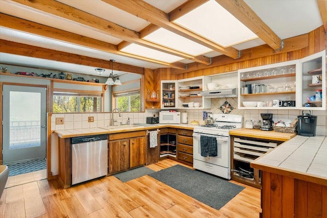 kitchen with a sink, white appliances, tile counters, backsplash, and under cabinet range hood