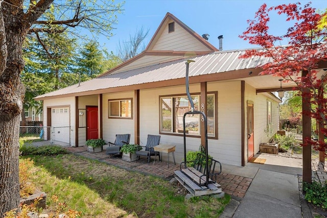 back of property featuring a porch, fence, an attached garage, and metal roof
