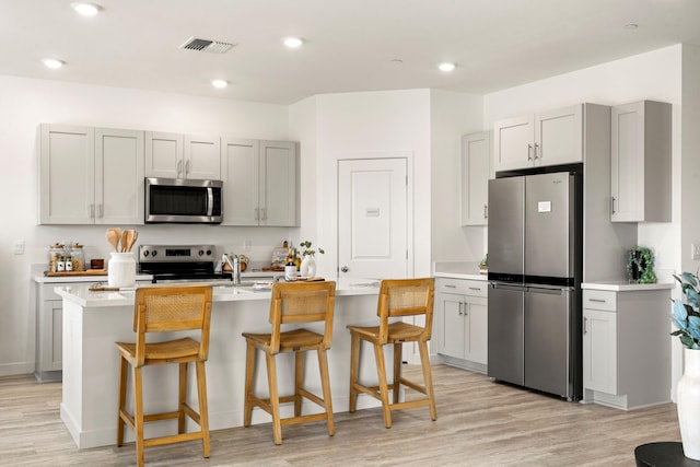kitchen featuring a kitchen bar, visible vents, light countertops, light wood-style floors, and stainless steel appliances