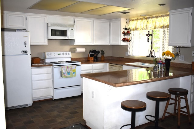 kitchen with white appliances, a sink, a peninsula, dark countertops, and white cabinets
