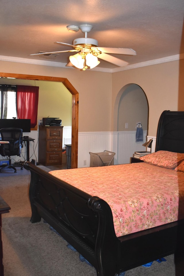 carpeted bedroom with a ceiling fan, wainscoting, and crown molding
