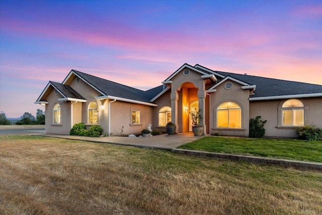 ranch-style house featuring roof with shingles, stucco siding, and a front lawn